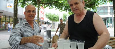 Ingo Wilke (rechts) verteilt an heißen Tagen Wasser in der Bahnhofstraße. Wer durstig ist, wie Bakri Nabin, bekommt einen Becher. Foto: Becker & Bredel.