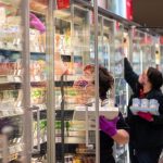 Mitarbeiterinnen in einem Supermarkt tragen Schutzmasken, während sie die Kühlregale mit Waren bestücken. Foto: Robert Michael/dpa-Zentralbild/dpa