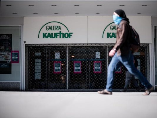 Ein Mann geht mit Mundschutz an einer Kaufhof-Filiale vorbei. Foto: Fabian Strauch/dpa/Archivbild